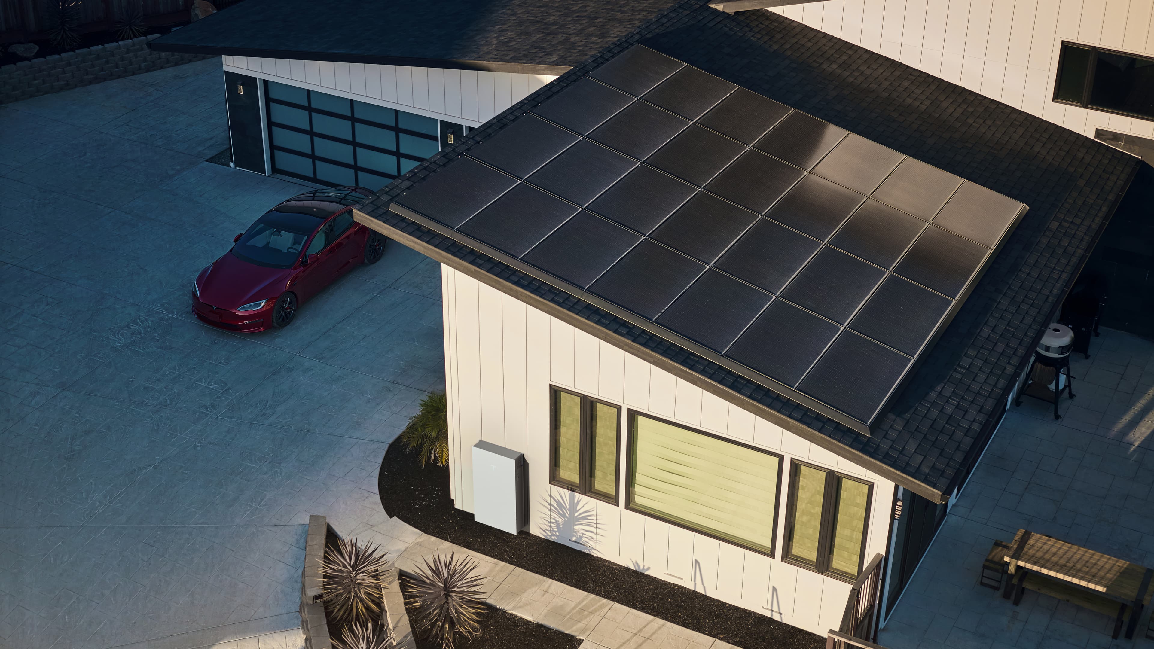 Aerial view of a home with rooftop solar panels and a Tesla Powerwall battery at dusk